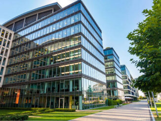 Beautiful glass office building with green grass and sidewalk in front.