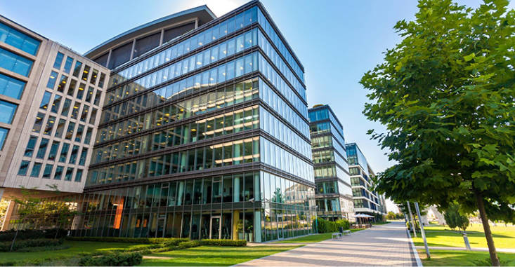 Beautiful glass office building with green grass and sidewalk in front.